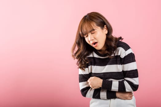 A woman in pain, an Asian portrait showing stomachache and abdominal suffering in a studio shot on a pink background. Conveying the concept of health and medical issues like gastritis.