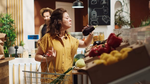 Vegan woman in eco friendly zero waste supermarket adding ethically sourced organic vegetables to shopping basket. Sustainable living client in local neighborhood shop picking farm grown groceries