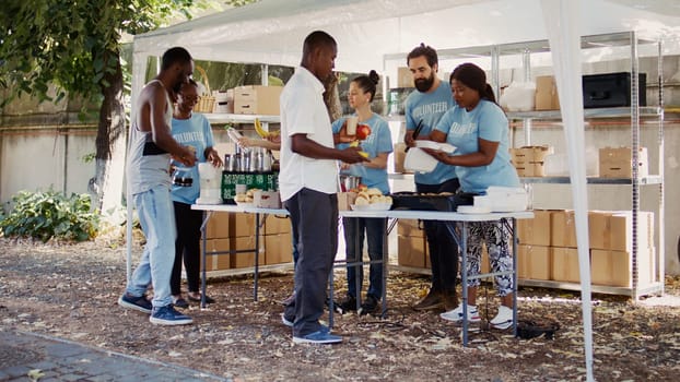 Multiracial volunteers engage in acts of charity by providing warm meals to underprivileged and homeless people. Non-profit group promote supportive atmosphere by extending essential aid to the poor.