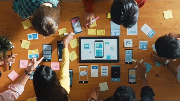 Top view of software developer team looking Ux Ui design for mobile phone interface from tablet while comparing and planning wireframe prototype designing together at creative workplace. Convocation.