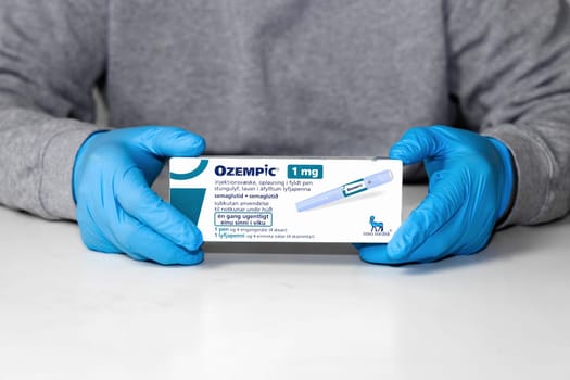 Hands in blue surgical gloves holds a package with Ozempic Insulin injection pen for diabetics. Denmark - February 10, 2024