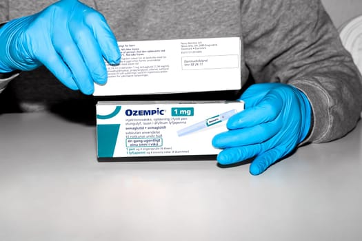 Hands in blue surgical gloves holds a package with Ozempic Insulin injection pen for diabetics. Denmark - February 10, 2024