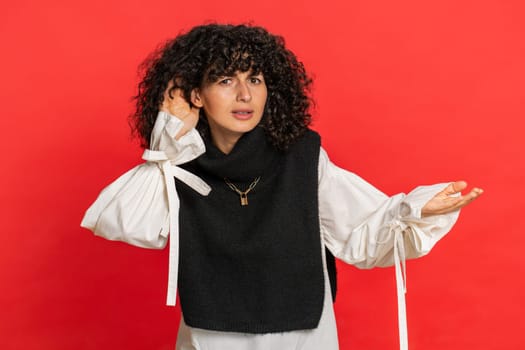 I cant hear you. What. Caucasian woman trying hear you looking confused and frowning keeping arm near ear for louder voice asking to repeat, to hear information deafness. Young girl on red background