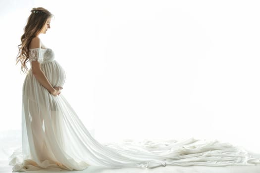 A pregnant woman stands in front of a white background wearing a white gown. The gown is long and flowing, and the woman is in a state of contemplation. Concept of serenity and contemplation