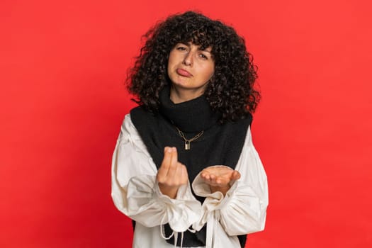 Give me money please. Caucasian young woman rubbing fingers show cash gesture demands to pay back the debt take loan do shopping begging investment reward. Girl isolated on studio red background