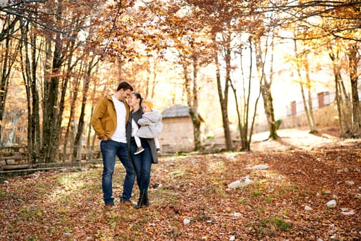 Dad touches his forehead with mom holding a little girl in her arms in the autumn forest. High quality photo