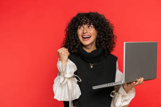 Happy excited Caucasian woman typing on laptop, working on project, enjoying results, winning lottery game celebrating success, online shopping victory good email news. Pretty girl on red background