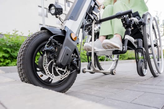 A faceless woman in a wheelchair with an assistive device for manual control. Electric handbike