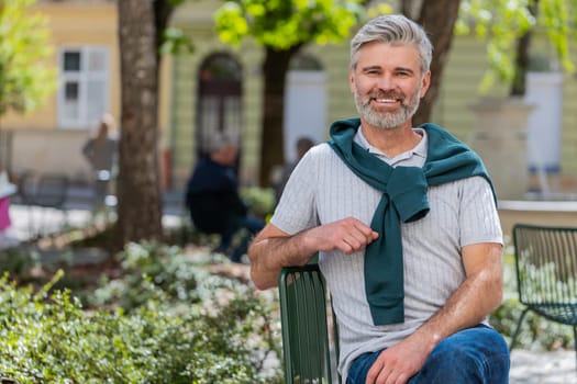 Portrait of happy bearded middle-aged man smiling friendly glad expression looking at camera dreaming resting relaxation feel satisfied good news outdoors. Guy in urban city sunshine street background