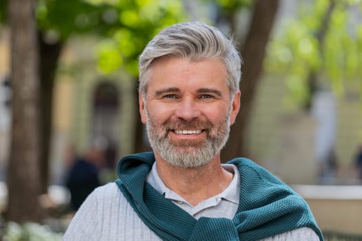 Portrait of happy bearded middle-aged man smiling friendly glad expression looking at camera dreaming resting relaxation feel satisfied good news outdoors. Guy in urban city sunshine street background