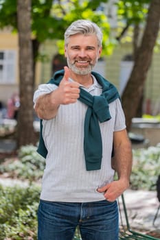 Like. Happy mature man tourist looking approvingly at camera showing double thumbs up positive something good positive feedback. Bearded guy standing on urban city street. Town lifestyles outdoors.