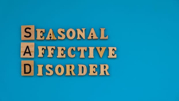 Seasonal affective disorder - text of wooden blocks on blue bright background. Concept of depression mood stress and anxiety. SAD wellbeing