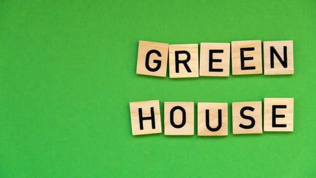 Green house text on wooden blocks on green background. Ecological concept Sustainable responsible living. Copy space. Single word