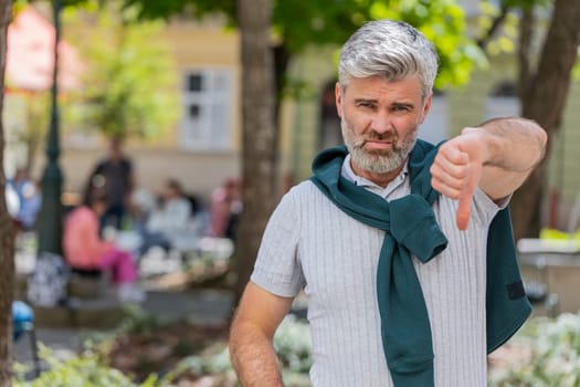 Dislike. Upset Caucasian man showing thumbs down sign gesture, expressing discontent, disapproval, dissatisfied bad work, mistake. Displeased mature guy male standing on urban city street outdoors.