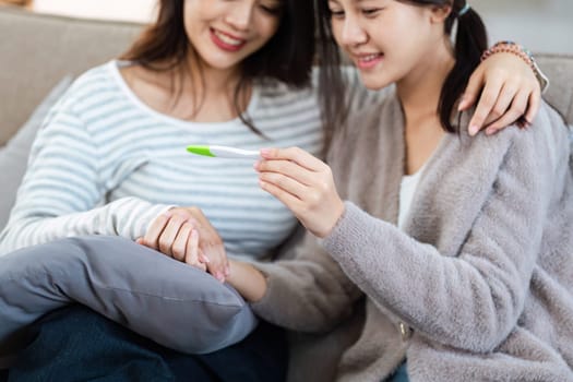 Two happy gay lesbian lgbt women couple sitting on sofa celebrating positive pregnancy test. lgbtq concept .