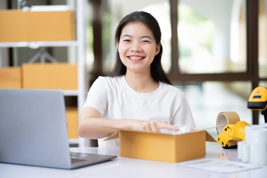 Young woman packing product for customer with cardboard box.