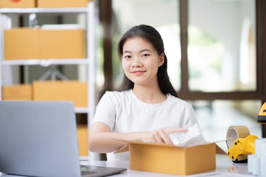 Young woman packing product for customer with cardboard box.