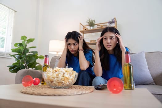 Lesbian couple anxiously watching Euro football match at home with popcorn and drinks. Concept of LGBTQ pride, sports enthusiasm, and domestic bonding.
