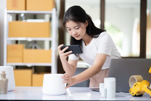 Young women taking photo of product with cell telephone or smartphone digital camera for post to sell online on the Internet and preparing pack product box. Selling online ideas concept