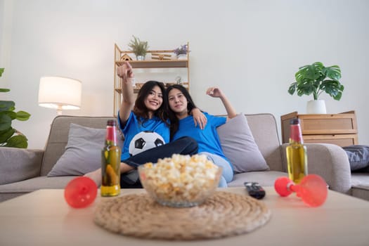 Lesbian couple cheering for Euro football at home with drinks and popcorn. Concept of LGBTQ pride, sports enthusiasm, and celebration.