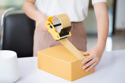 Young Asian business entrepreneur sealing a box with tape. Preparing for shipping, Packing, online selling, e-commerce concept.