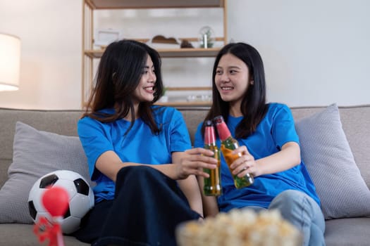 Lesbian couple cheering for Euro football with beers at home. Concept of LGBTQ+ pride, celebration, and sports enthusiasm.