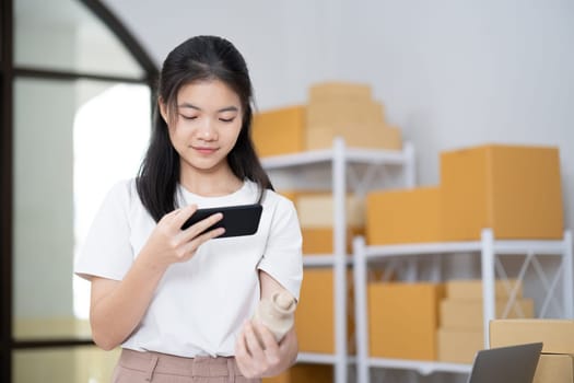 Young women taking photo of product with cell telephone or smartphone digital camera for post to sell online on the Internet and preparing pack product box. Selling online ideas concept