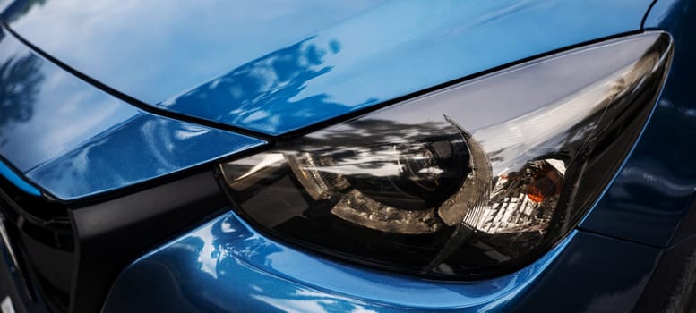 Blue car's modern xenon headlight lamp. Reflective chrome design safety technology for night driving. Clean shiny and luxury sedan headlight in industry. Detail on one of the LED car headlights