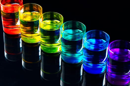 Colorful small glasses on black background with alcohol drink close up