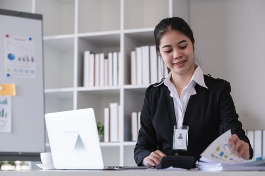 Accountant sitting with financial documents, using laptop, calculating financial and tax figures for company on table in office.