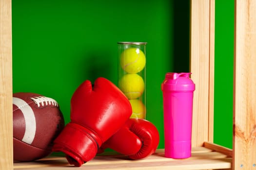 Shelves with different sports equipment against green wall close up