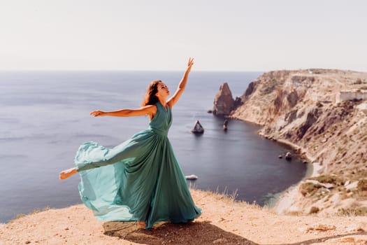 Woman green dress sea. Female dancer posing on a rocky outcrop high above the sea. Girl on the nature on blue sky background. Fashion photo