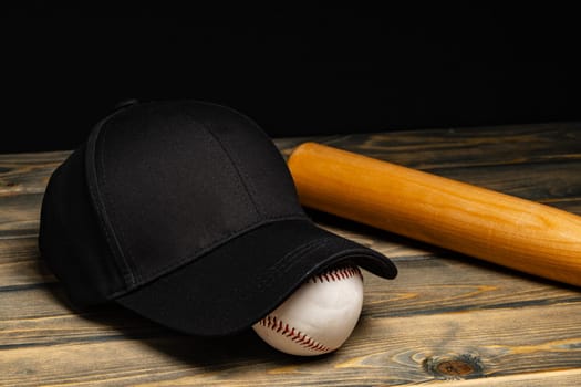 Baseball cap, ball and bat on wooden background close up