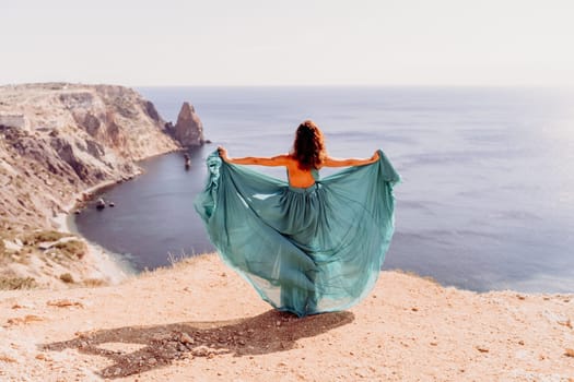 Woman green dress sea. Female dancer posing on a rocky outcrop high above the sea. Girl on the nature on blue sky background. Fashion photo