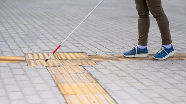 Close-up of a woman's legs with a cane near a tactile tile