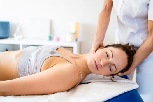 Calm female patient getting treatment in manual therapy clinic while physiotherapist doing massage of neck in hospital room