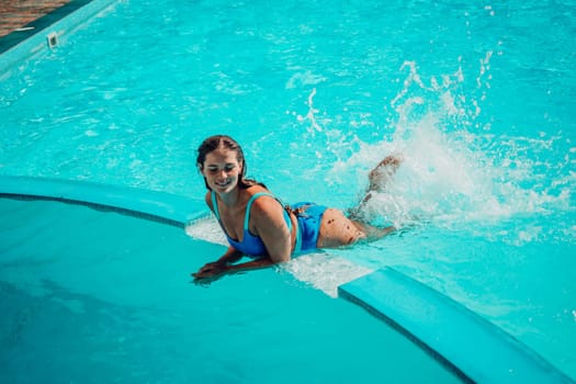 A woman is in the water, smiling and enjoying herself. The water is blue and the pool is surrounded by a white ledge