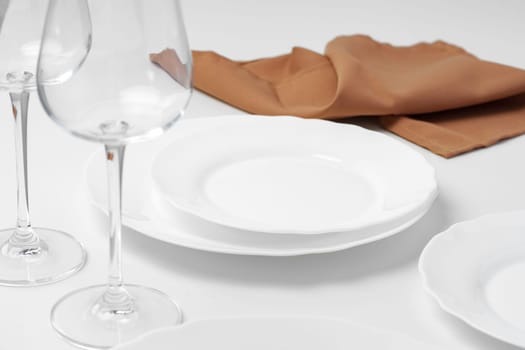 Stylish table setting with white dishware on white tablecloth close up