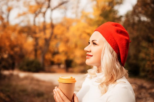 A blonde woman wearing a red hat is holding a coffee cup. She is smiling and looking out into the distance