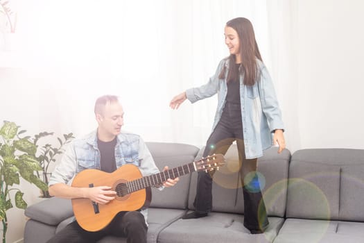 Father guy teaching girl teenager daughter guitar playing at home. Family musical lessons with strings instrument. High quality photo