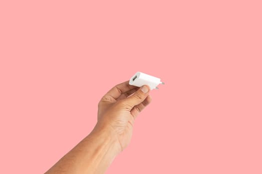 Black male hand holding a USB charger plug isolated on pink background. High quality photo