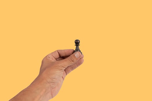 Isolated hand holding a chess figure on yellow background. High quality photo