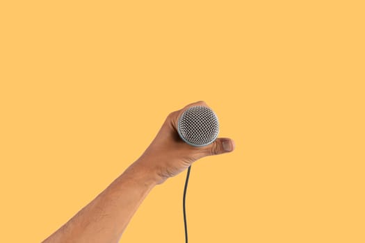 Black male singer hand holding a microphone isolated on yellow background. High quality photo