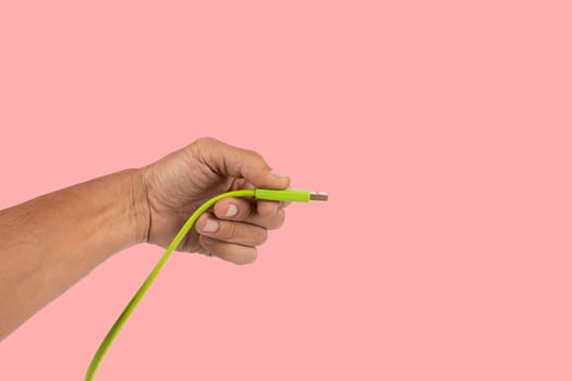 Black male hand holding a green USB cable isolated on pink background. High quality photo
