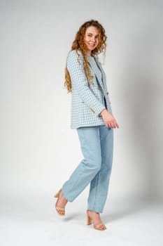 Young woman with curly hair in blue jacket posing on gray background close up