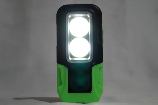 A green and black flashlight with two white lights. High quality photo
