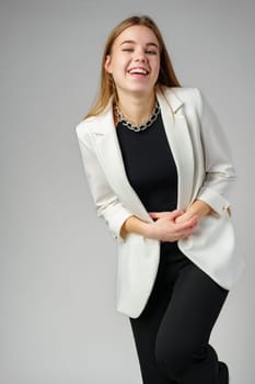 Smiling Young Woman in a White Blazer Posing Against a Grey Background close up