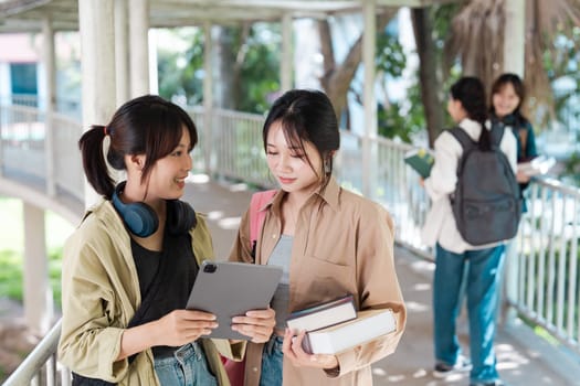 asian student socializing with tablet and books on campus walkway. university concept.