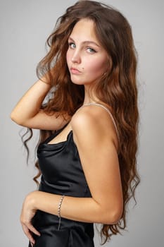 A woman wearing a black dress strikes a pose for a photograph, looking elegant and stylish in her attire. The backdrop is simple, allowing her to be the focal point of the image.