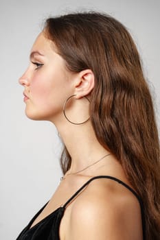 A woman with long flowing hair is depicted wearing oversized hoop earrings. The womans hair cascades down her shoulders, framing her face as the earrings dangle elegantly.
